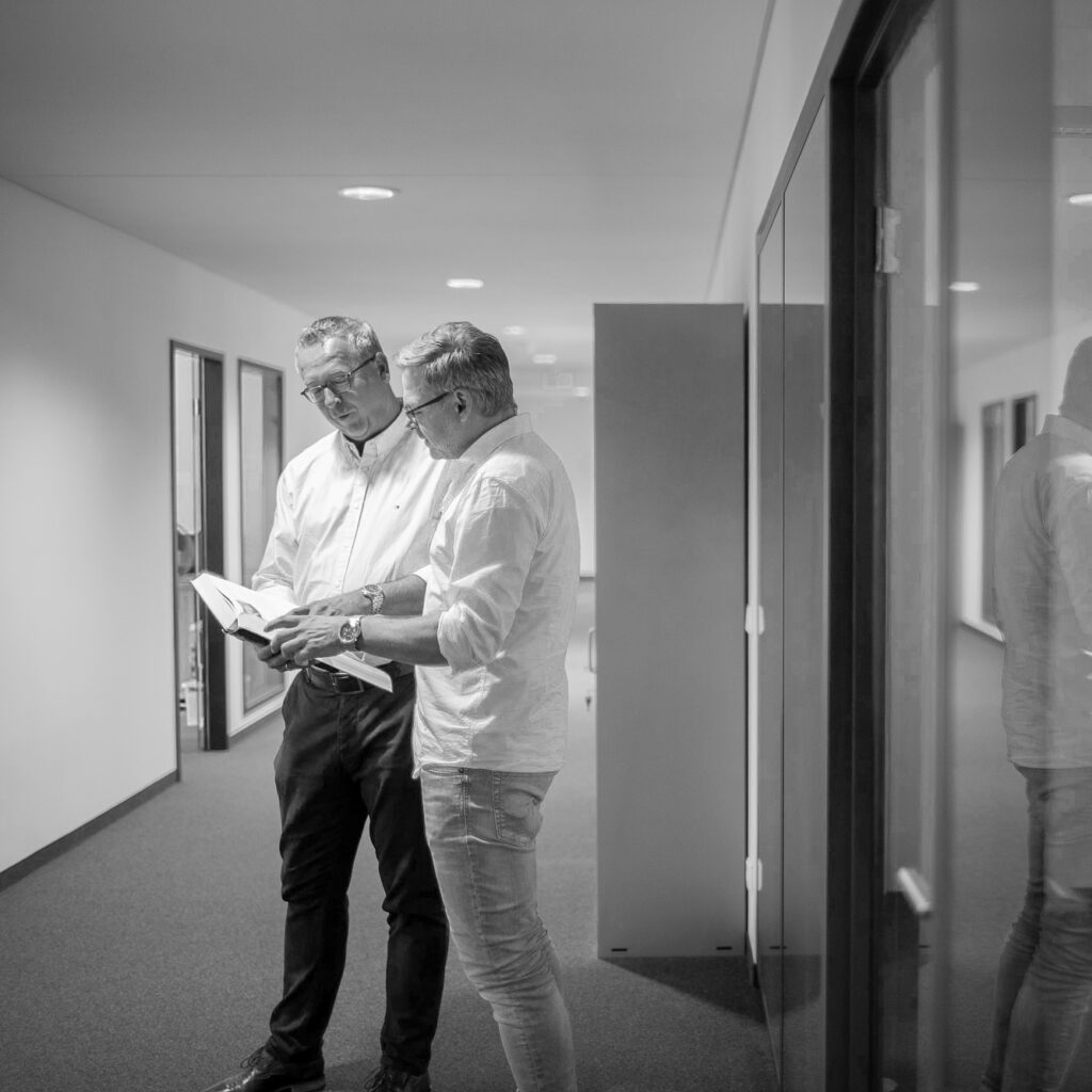 Zwei innovas-Mitarbeitende im Gespräch auf dem Gang vor einem Büro mit Glasfront
