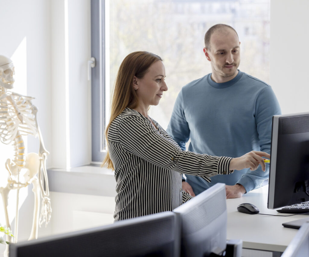 Zwei innovas-Mitarbeitende im Vodergrund besprechen sich, während im Hintergrund ein Schulungsskelett steht.