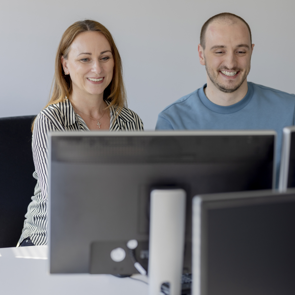 VBG Zwei innovas-Mitarbeitende sitzen vor einem Monitor.