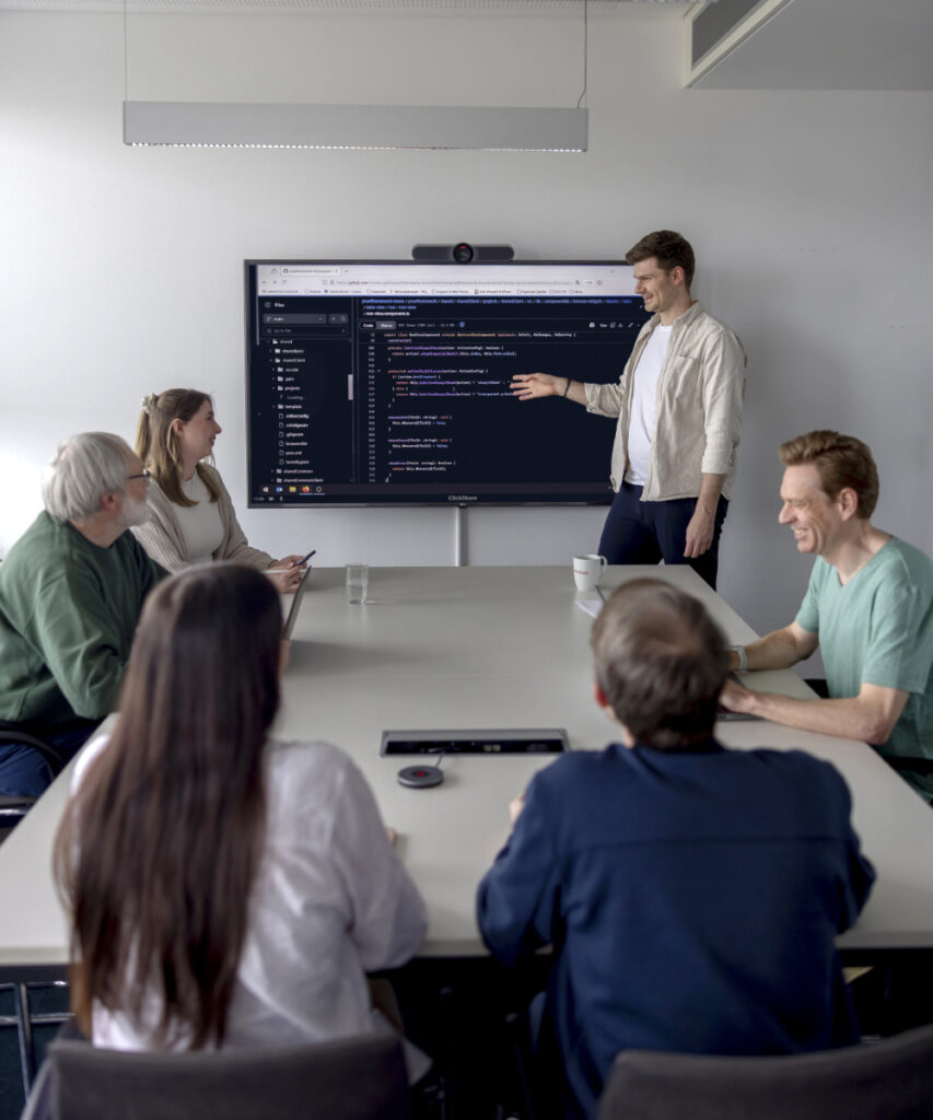 Eine Meetingsituation mit verschiedenen innovas-Mitarbeitenden vor einem großen Monitor.