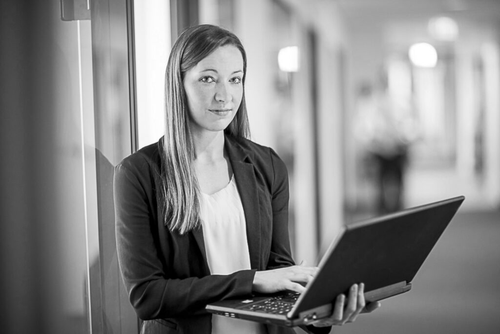 Eine innovas-Mitarbeitende steht mit ihrem Laptop auf dem Gang