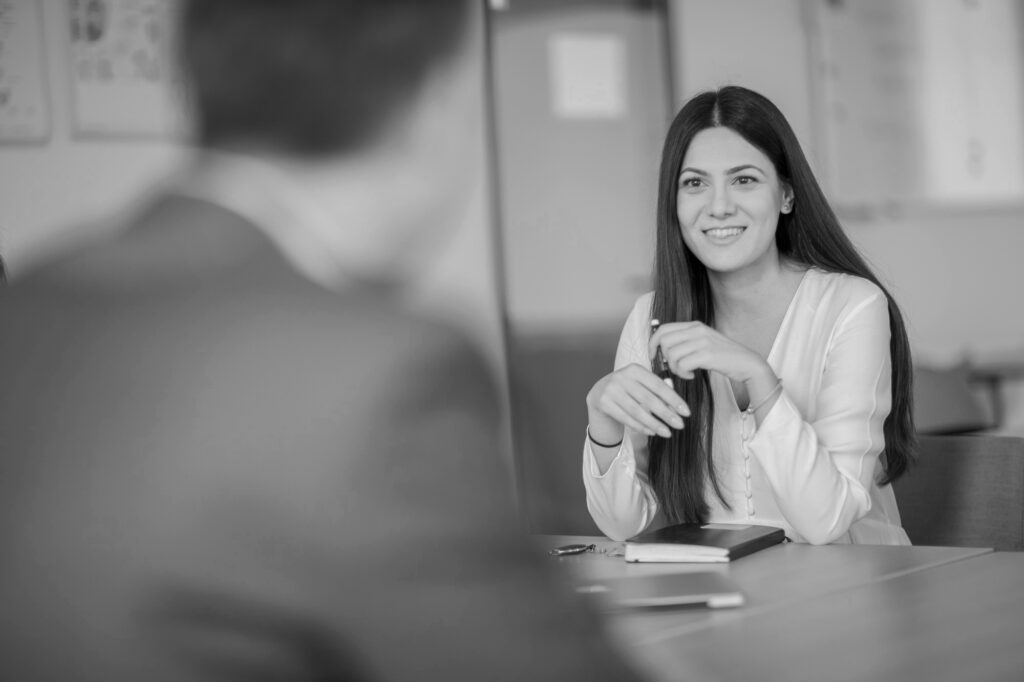 Eine innovas-Mitarbeitende sitzt an einem Besprechungstisch und ist im Gespräch mit einer anderen Person