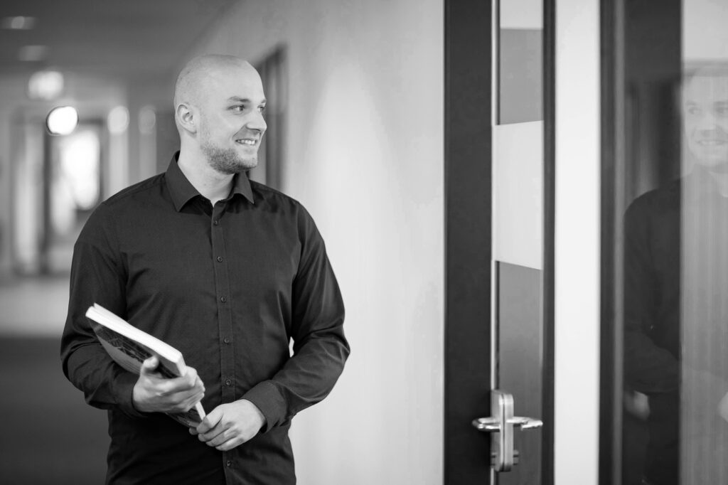 Ein innovas-Mitarbeitender steht mit einem Fachbuch auf dem Gang und schaut in ein Büro