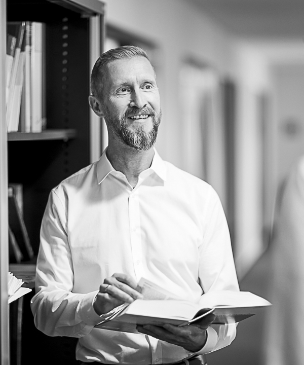 Ein innovas-Mitarbeitender steht mit einem offen Buch vor einem Regal und ist im Gespräch mit einer anderen Person.