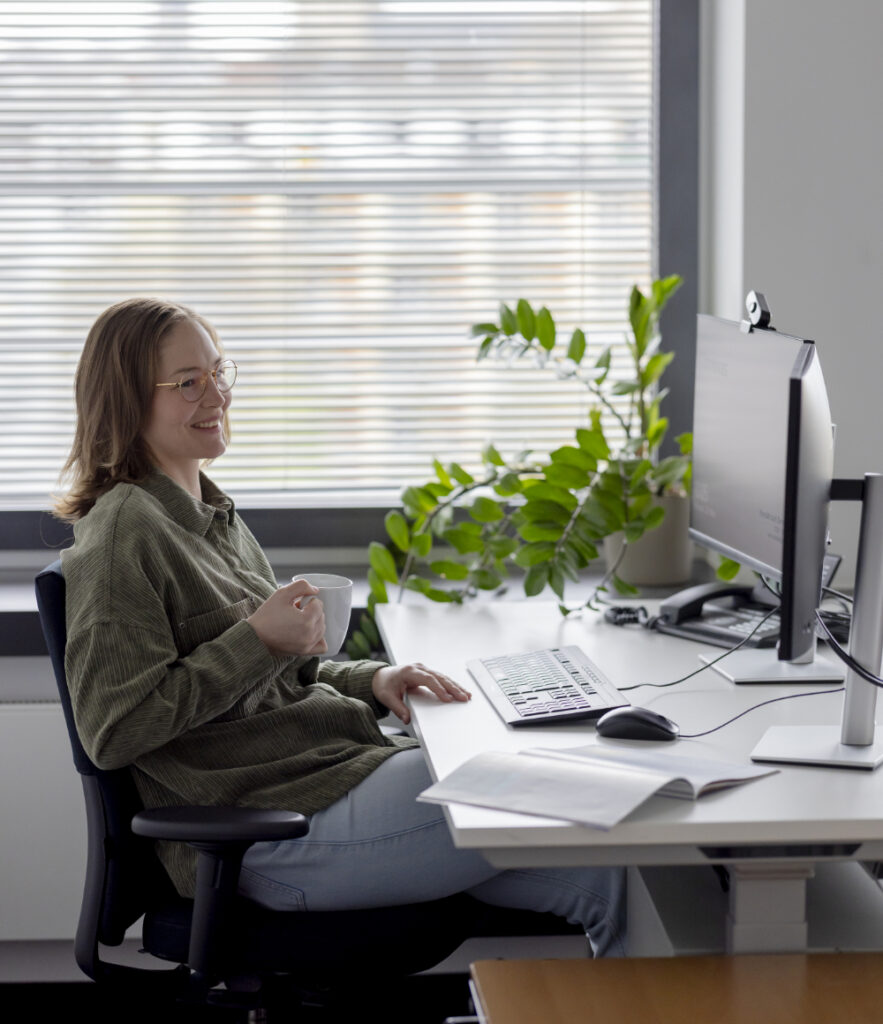 Eine innovas-Mitarbeitende sitzt mit einer Tasse an ihrem Schreibtisch.