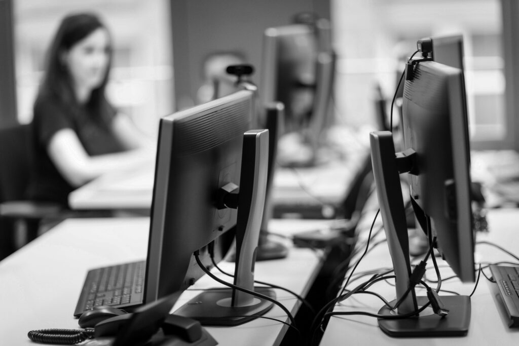 Im Vordergrund steht ein Monitor mit Telefon und im Hintergrund sitzt eine innovas-Mitarbeitende  an ihrem PC