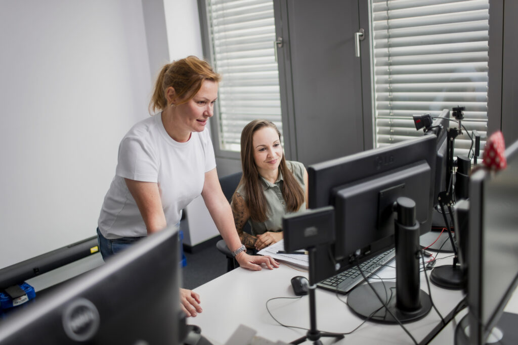 Zwei innovas-Mitarbeitende beschrechen sich an einem Arbeitsplatz.