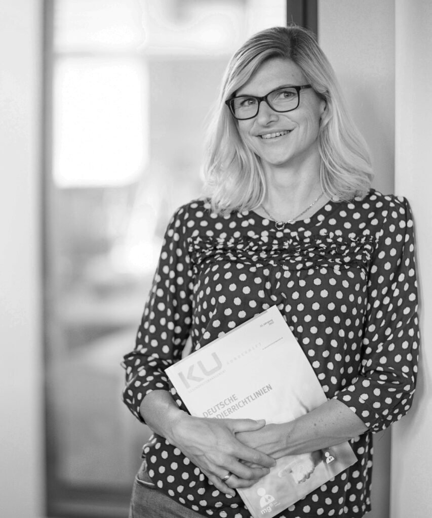 Eine innovas-Mitarbeitende steht mit einer Ausgabe der Deutschen Kodierrichtlinien vor ihrem Büro