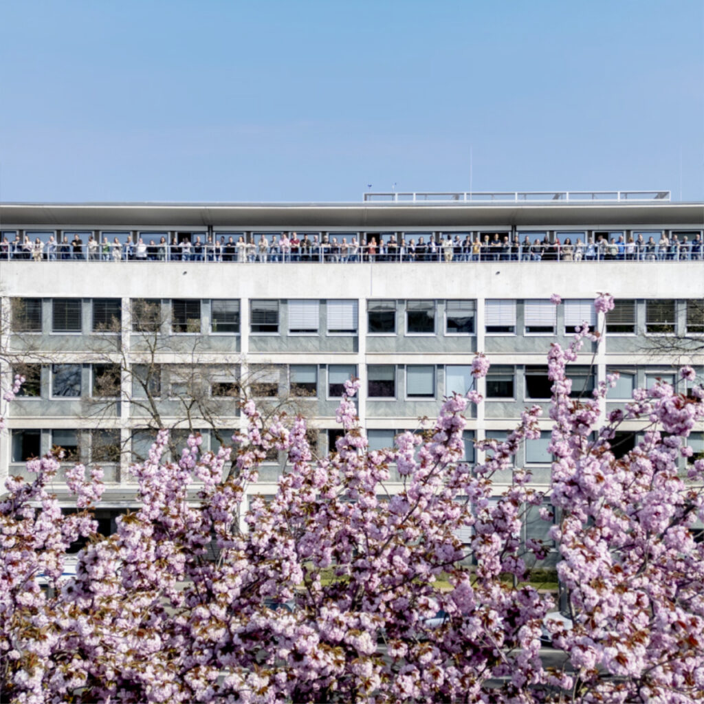 Das Firmengebäude mit den Kirschbäumen im unteren Bereich und einigen innvas-Mitarbeitenden auf der oberen Terrasse.