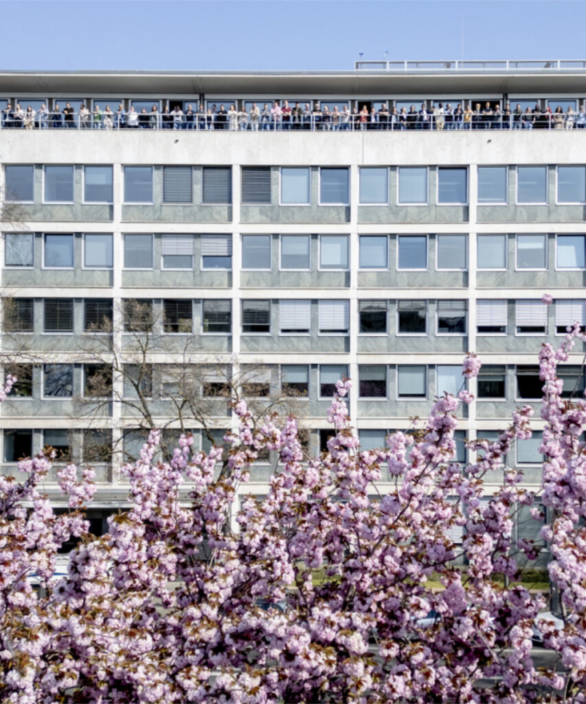 Das Firmengebäude mit den Kirschbäumen im unteren Bereich und einigen innvas-Mitarbeitenden auf der oberen Terrasse.